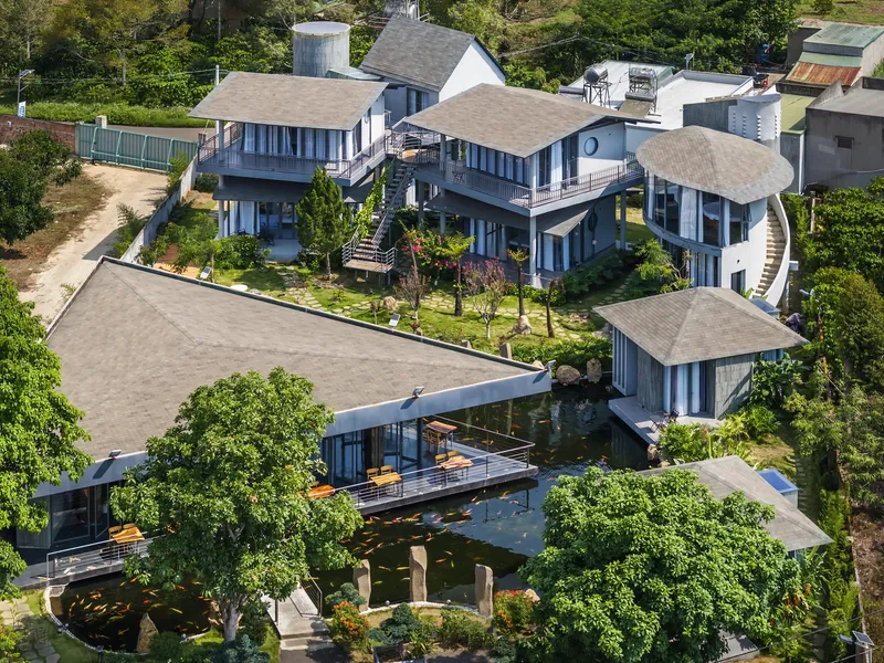 Aerial view of the clustered volumes with grey tiled roofs amid landscaped gardens and trees