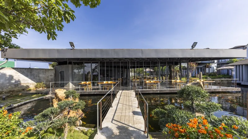 Concrete slab roof sheltering a glass pavilion with a timber walkway crossing a pond with planted islands