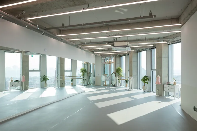 Open interior space with exposed concrete ceiling, linear lighting, and floor-to-ceiling windows casting sunlight