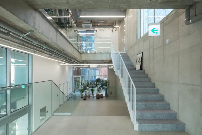 Terrazzo staircase with white railings rising past exposed concrete walls and suspended linear lights