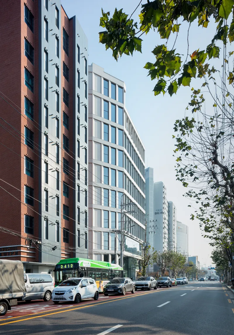 Curved white facade along a tree-lined street with parked cars under overhanging green foliage
