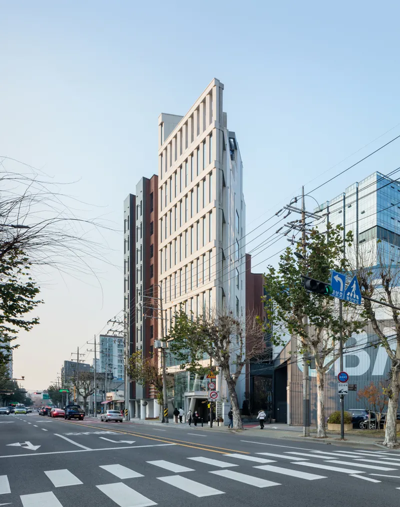 Street view of the angular white facade rising above a pedestrian crossing with bare winter trees