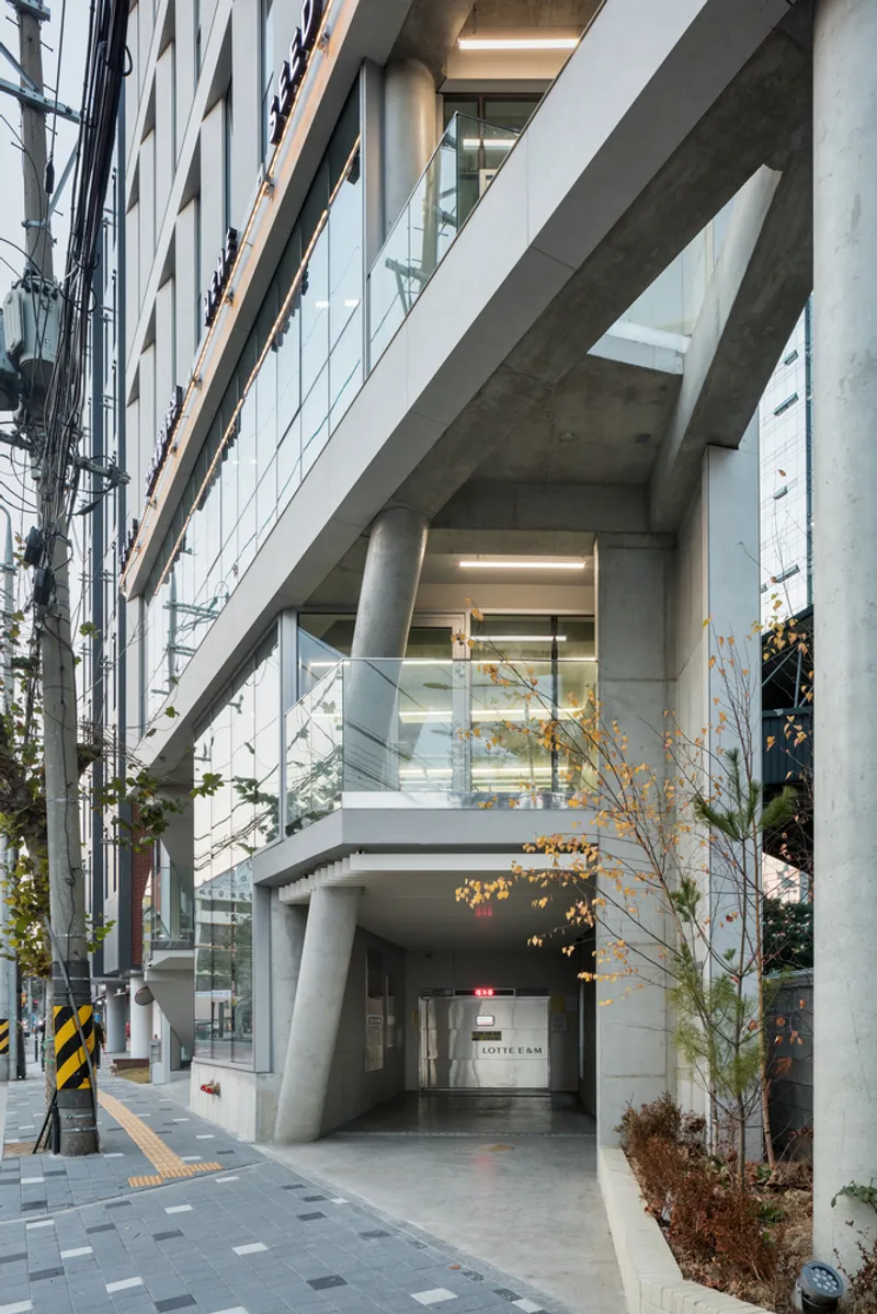 Ground level entrance with angled concrete columns framing a glass passage beneath the cantilevered volume