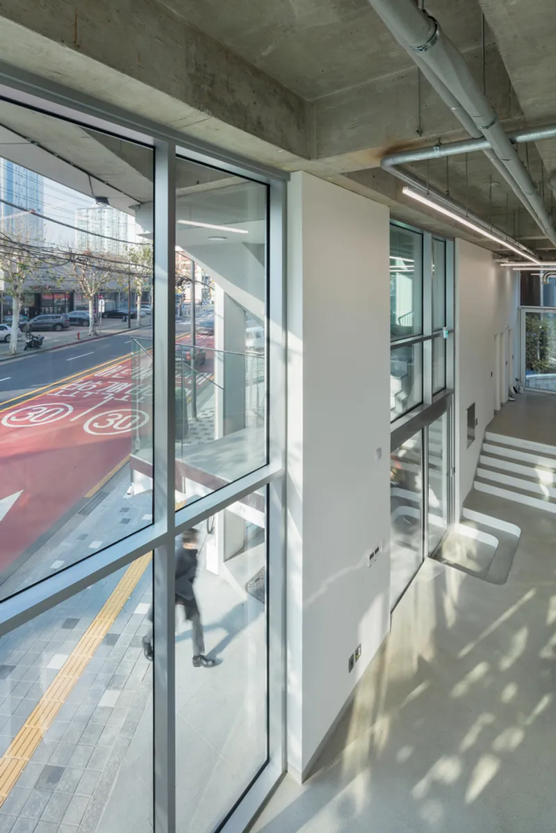 Interior lobby with full-height glazing and exposed concrete ceiling bathed in morning sunlight