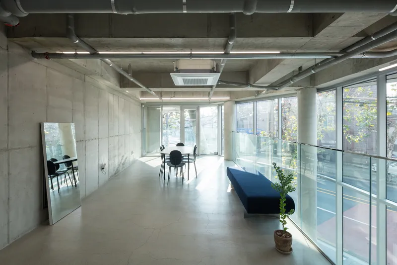 Minimalist interior with concrete storage wall, glass balustrade, and blue bench beside full-height glazing overlooking trees