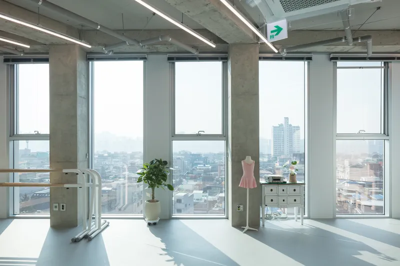 Open studio space with exposed concrete ceiling, floor-to-ceiling windows, and a dress form near a hazy urban skyline