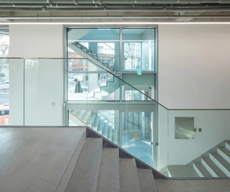 Glass-enclosed stairwell connecting multiple levels with white walls and terrazzo flooring in daylight