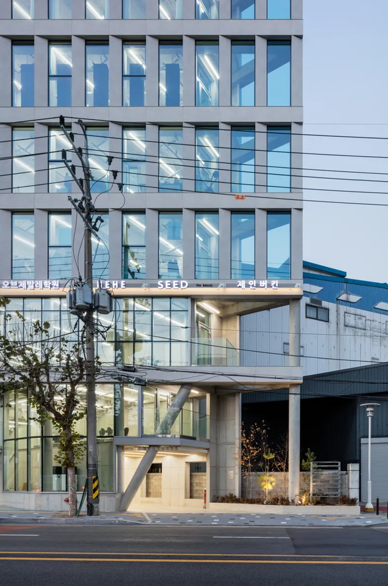 Street view of a glass and metal panel facade with exposed concrete circulation core at dusk