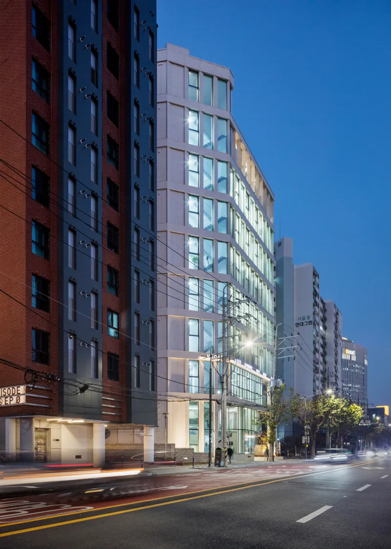 Corner facade with prefabricated cladding panels and continuous ribbon windows illuminated at twilight