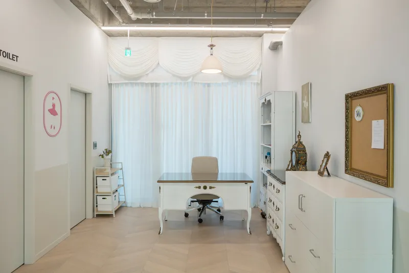 Office interior with white desk, sheer curtains and exposed concrete ceiling with suspended lighting