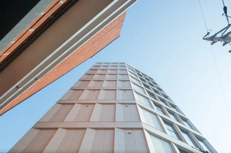 Upward view of the tower facade with alternating pink panels and glazing under clear sky