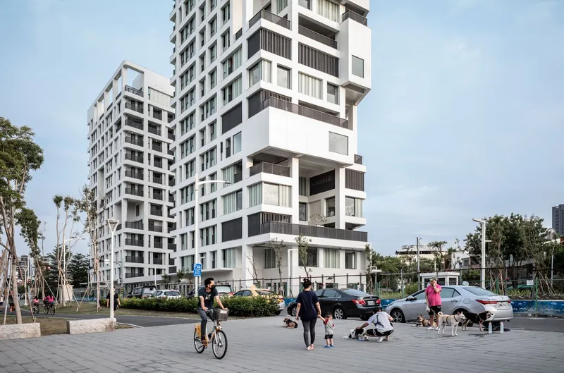 Staggered white facade with projecting balconies viewed from the public plaza with cyclists and pedestrians