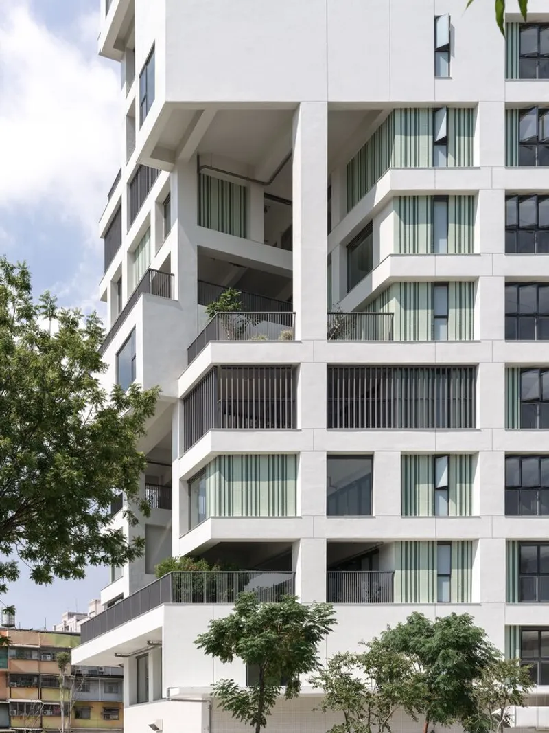 Offset balconies with vertical screen panels and planted terraces framed by mature trees below