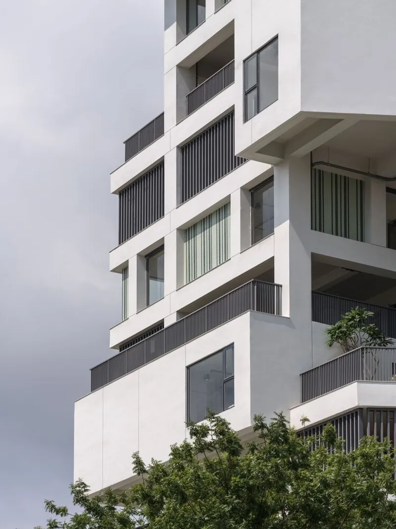 Alternating balconies with dark vertical screening and recessed glazing beneath an overcast sky
