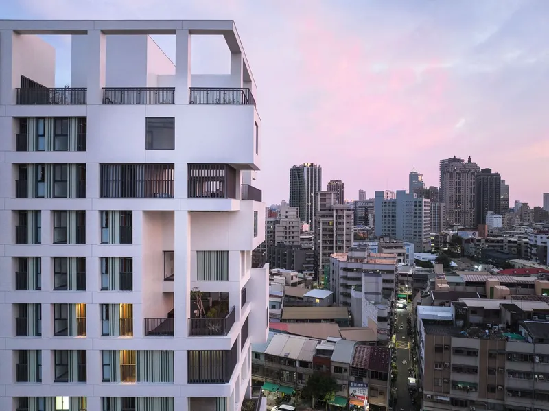 White tower facade with varied window openings at dusk overlooking dense urban skyline