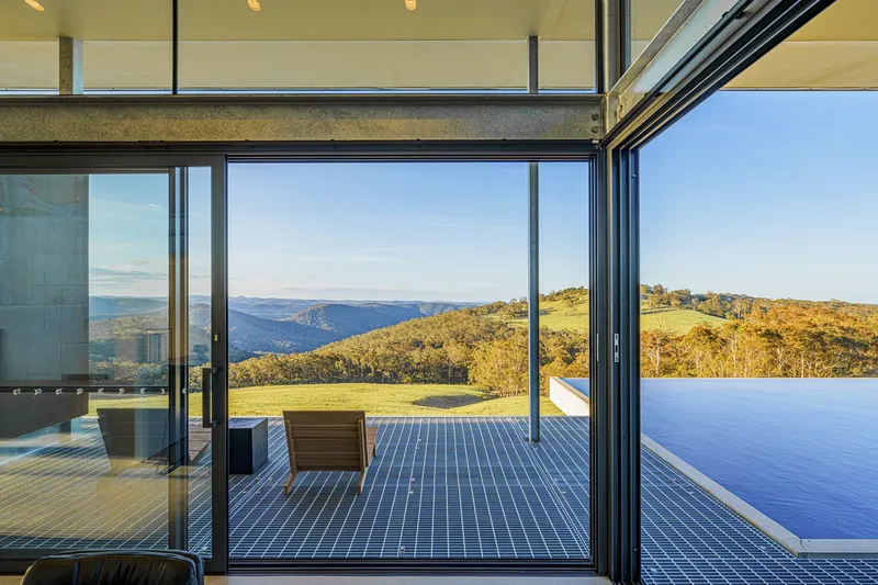 Floor-to-ceiling glazing framing the terrace, infinity pool and distant mountain ridges in afternoon light