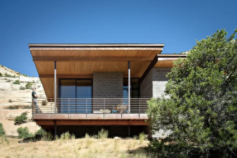 Elevated timber and concrete block residence with horizontal railing deck overlooking a sloping desert hillside