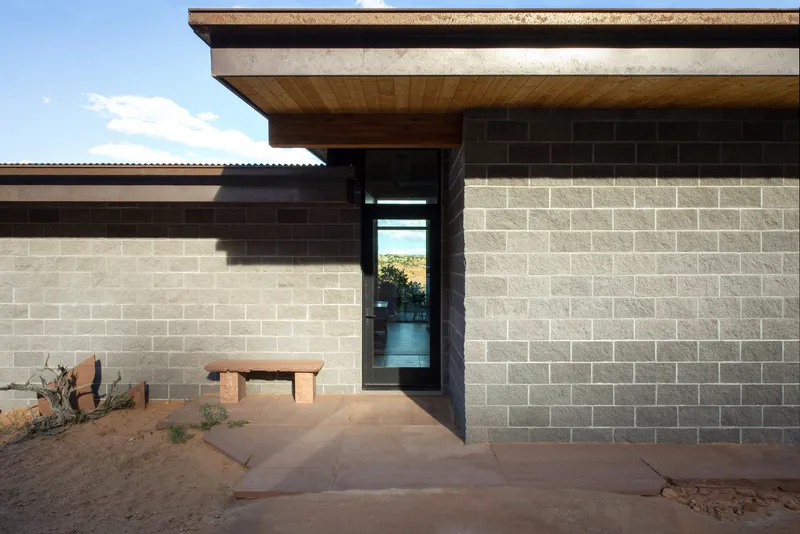 Entry facade with two-tone concrete block walls and narrow glazed slot opening beside timber soffit overhang