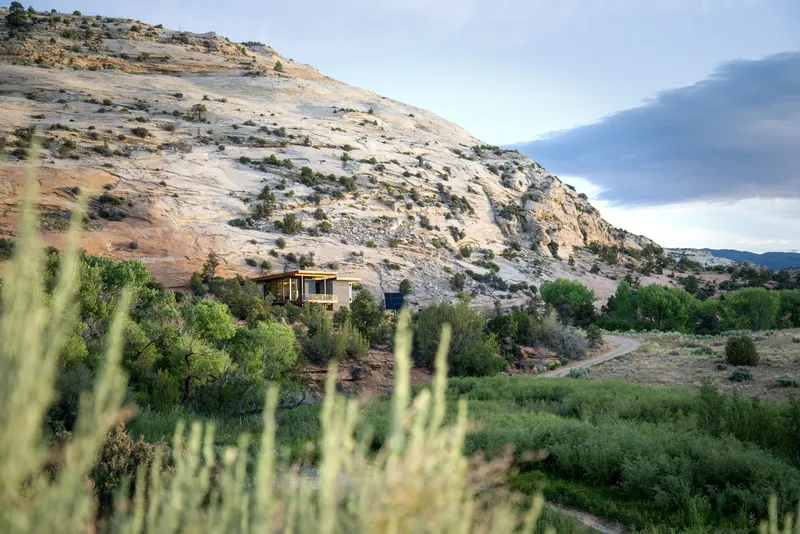 Distant view of the residence nestled among trees at the base of layered sandstone formations