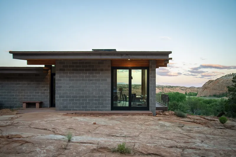 Grey concrete block facade with timber soffit and glazed entry opening at dusk