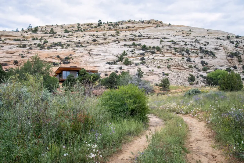 Distant view of the residence nestled among native grasses and shrubs beneath a massive sandstone outcrop