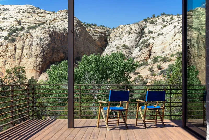 Timber deck with two blue canvas chairs facing the canyon through a steel railing and glass doors