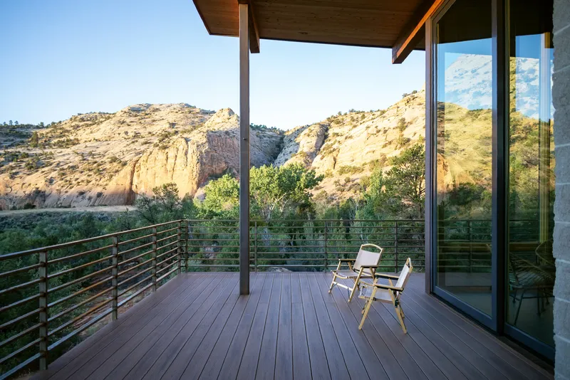 Covered deck with horizontal steel railing and two chairs facing the desert canyon landscape