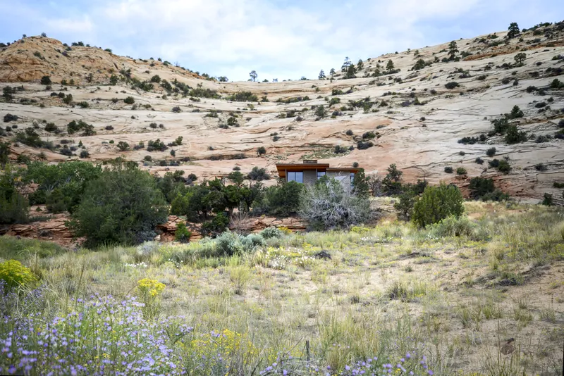 The low-slung structure set among wildflowers and grasses with layered rock formations rising behind