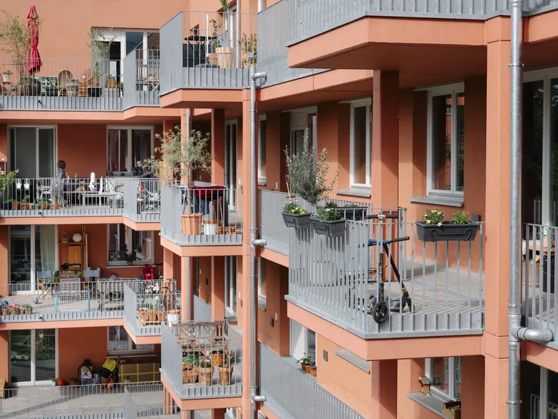 Stacked balconies with corrugated metal railings and potted plants on terracotta-framed residential units in daylight