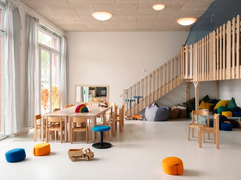 Childcare playroom with timber vertical screen, light wood furniture, toys scattered on pale resin flooring and recessed ceiling lights