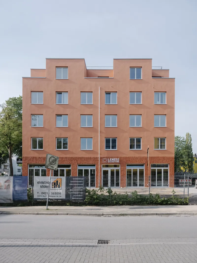Street facade with terracotta plaster, punched windows, stepped parapet, and ground-floor retail beneath an overcast sky