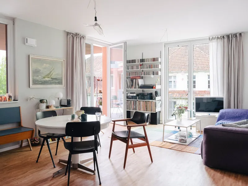Open living and dining area with oak flooring, glass doors to balcony, and bookshelves along white walls