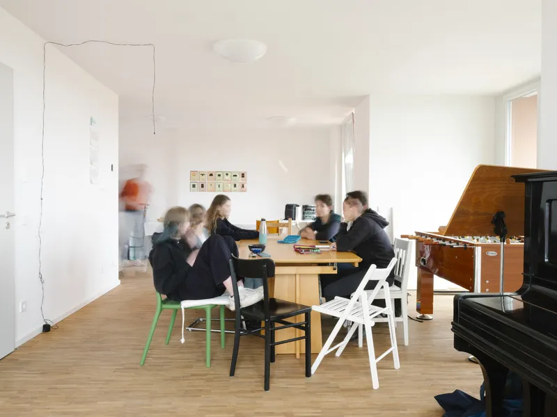 Open living space with family gathered around a wooden dining table near a piano