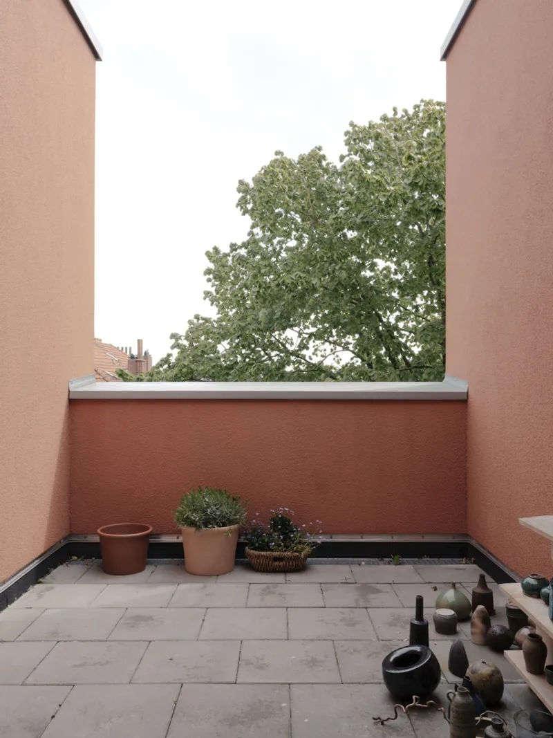 Private terrace with terracotta walls and potted plants framed by a mature tree beyond