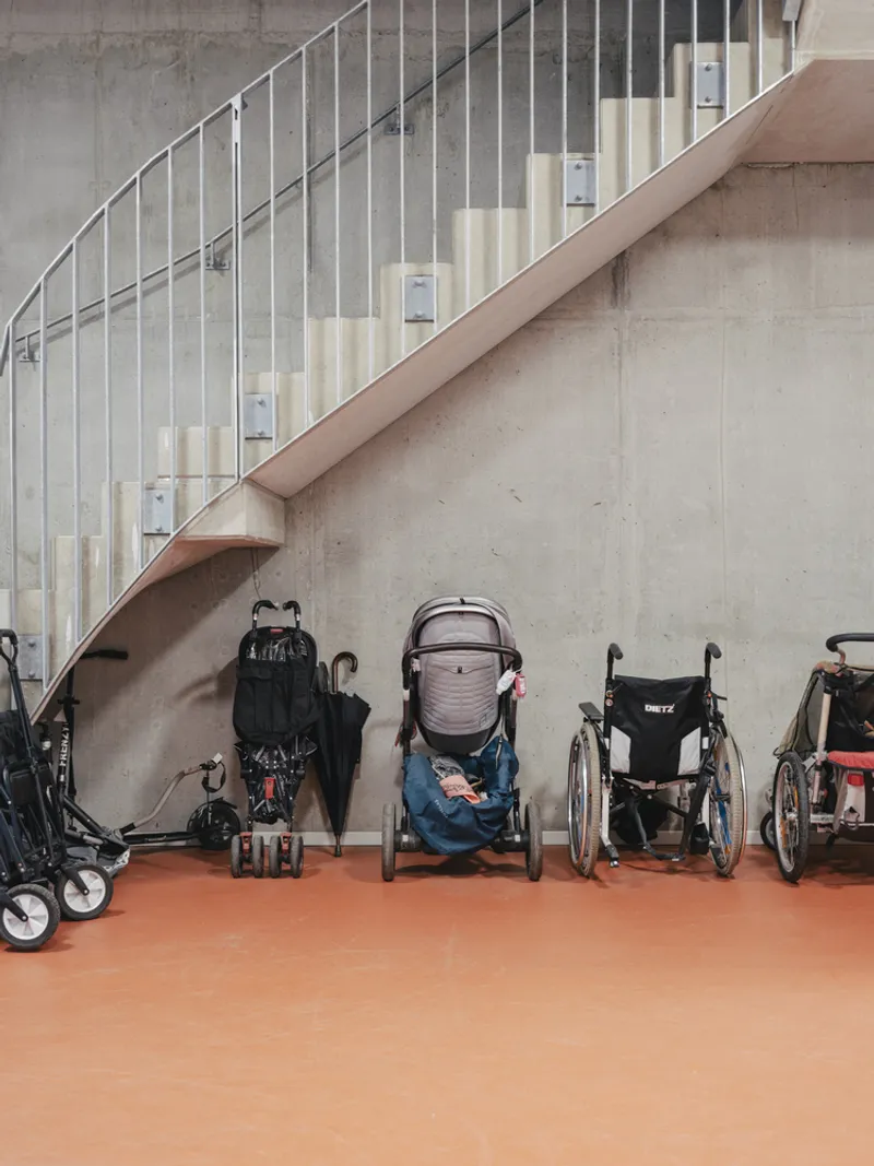 Ground floor stair with vertical metal balustrades above wheelchairs and strollers on orange flooring