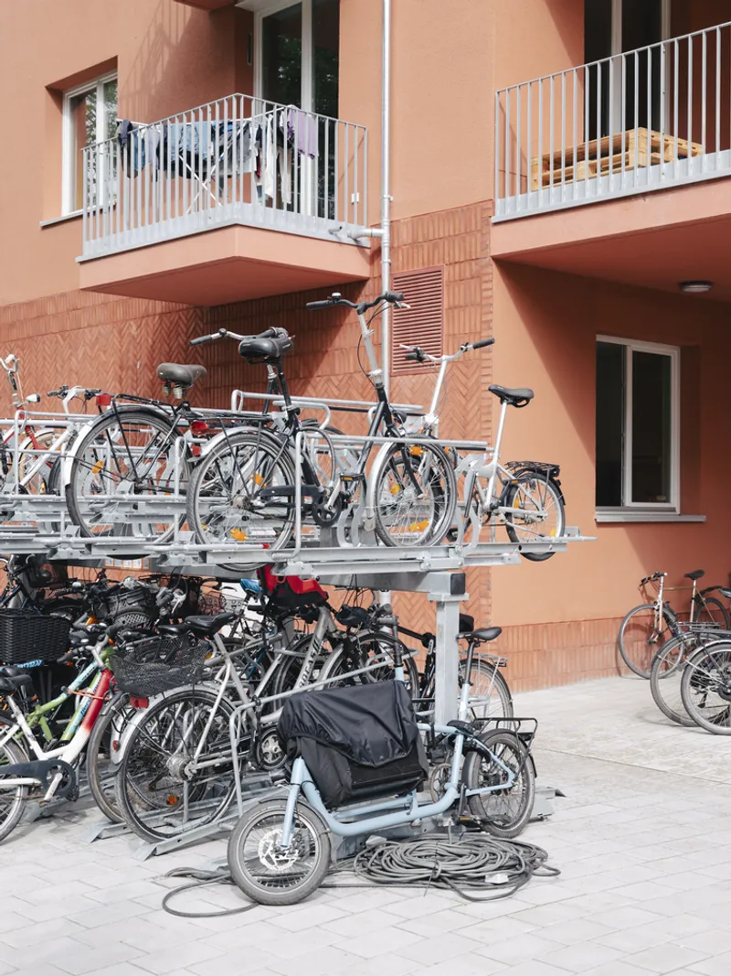 Two-tier bicycle parking racks filled with bikes beneath residential balconies with white railings