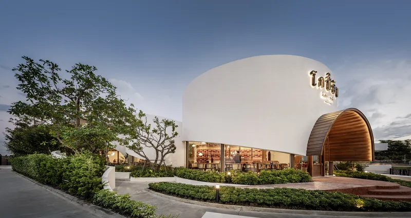 Curved white structure with illuminated arched entrances and planted beds in early evening light