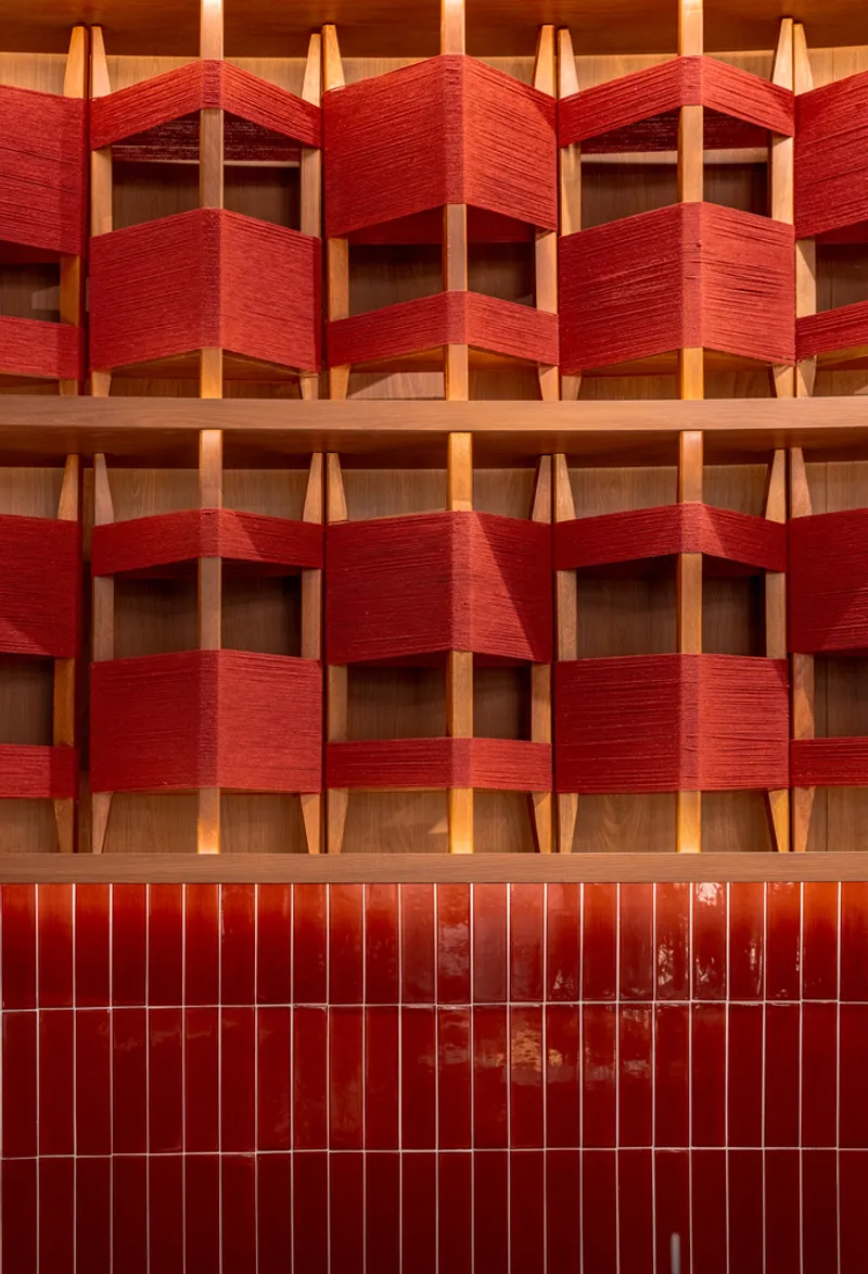 Facade detail with woven red textile panels wrapped around timber frames above a red tiled base