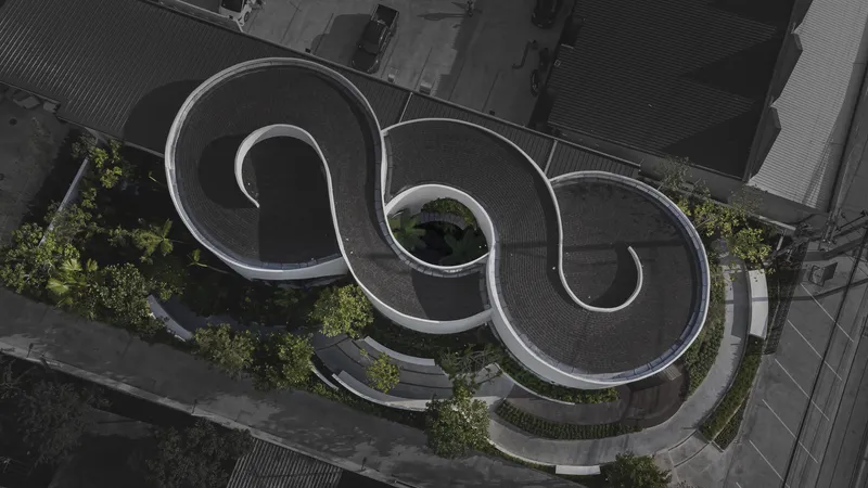Aerial view of three spiral-shaped roof volumes with planted courtyards and paving between neighboring buildings