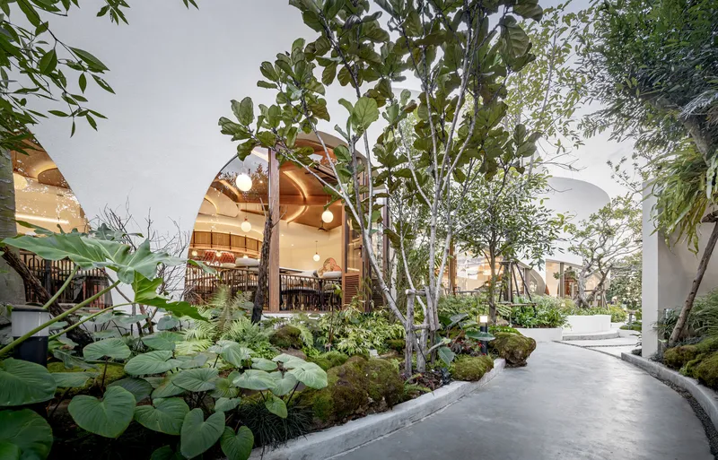 Curving pathway through planted garden with arched timber-framed pavilions illuminated in evening light
