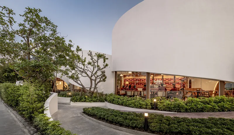 Curved white facade with arched glass openings overlooking landscaped terrace with trees at twilight