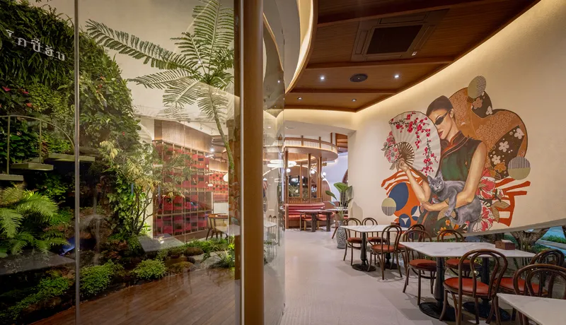 Dining space with glass-enclosed planted courtyard and wall mural of figures in traditional dress