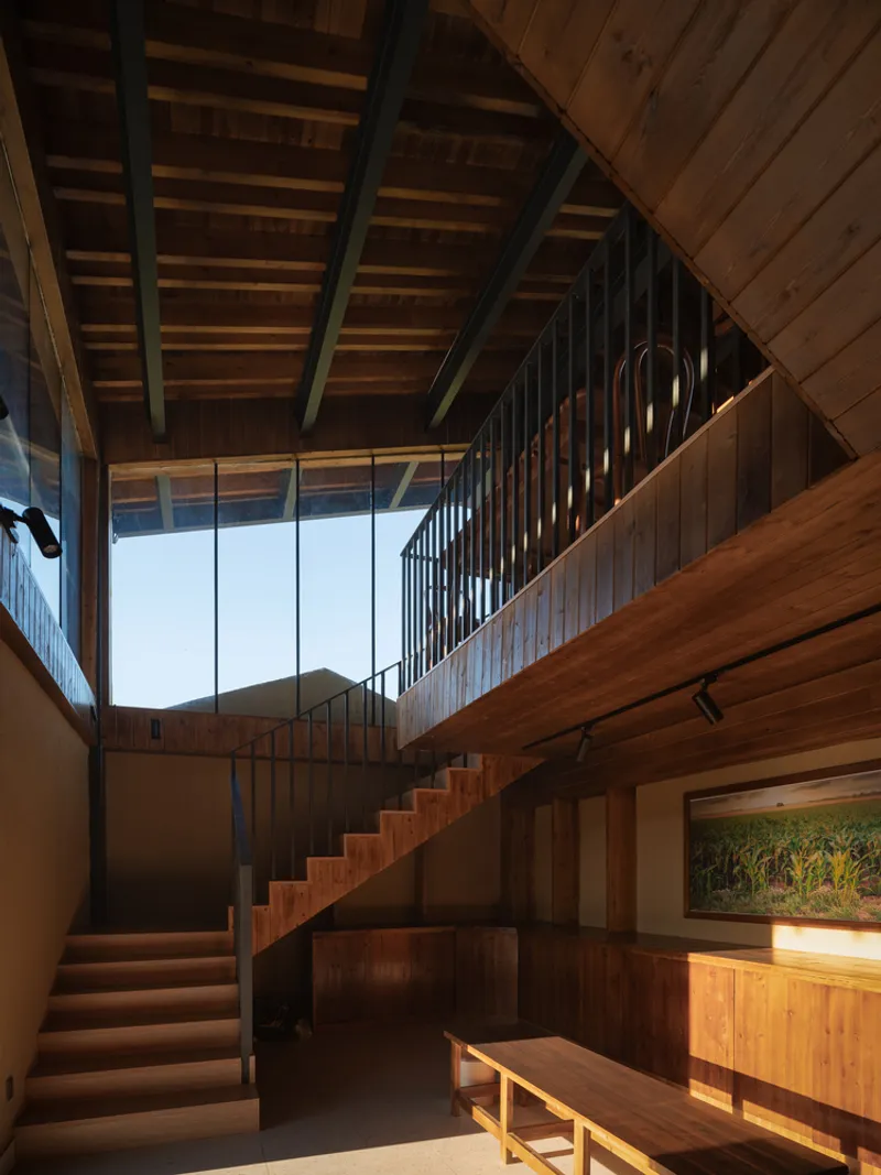 Double-height stairwell with timber treads and black steel railings beneath a skylight at dusk