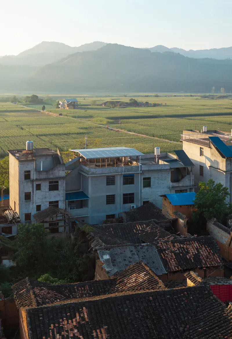 Aerial view of concrete and brick village rooftops with mountains and agricultural fields in morning mist