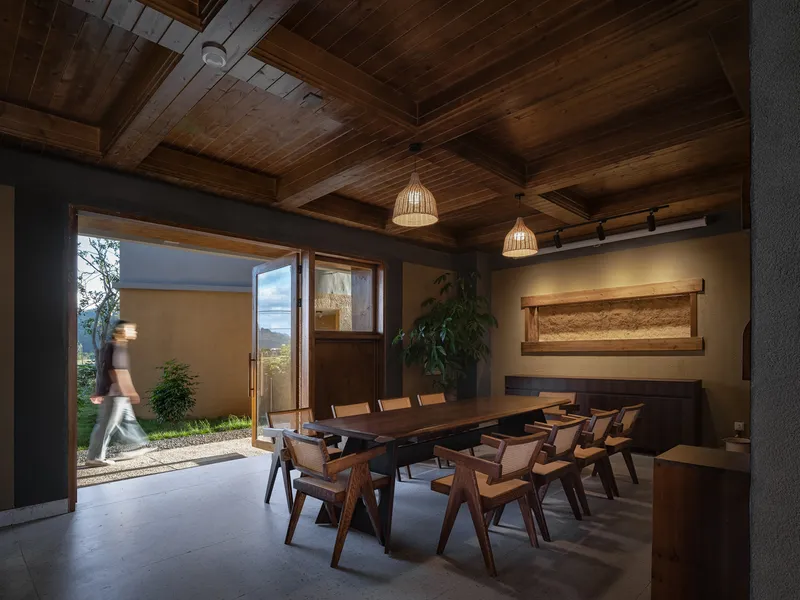 Dining room with exposed timber ceiling and open doors leading to a courtyard with a figure passing through