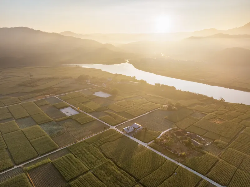 Aerial view of structures surrounded by gridded agricultural fields beside a river at sunrise