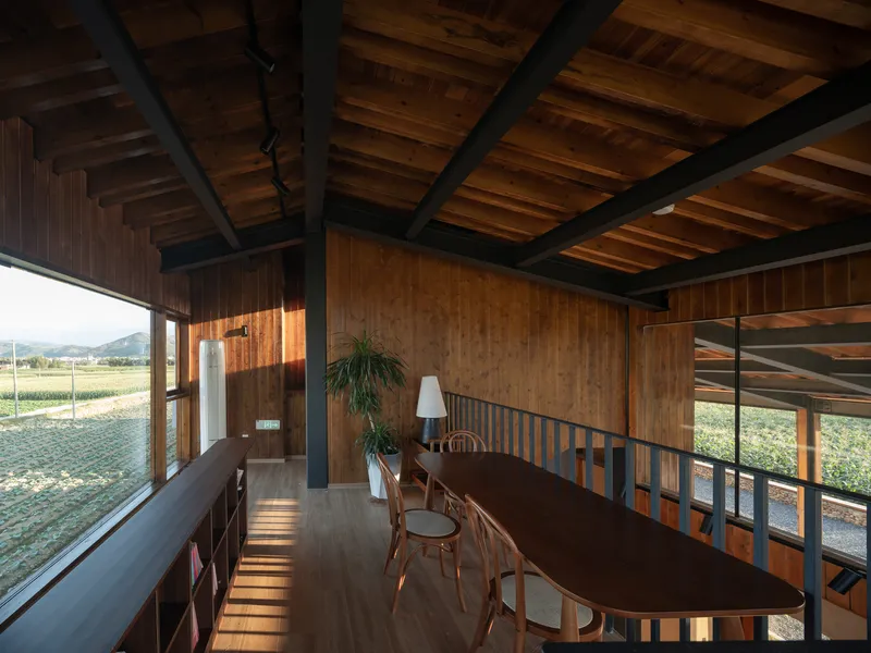 Dining space with exposed timber ceiling beams and metal railings overlooking the landscape through full-height glazing