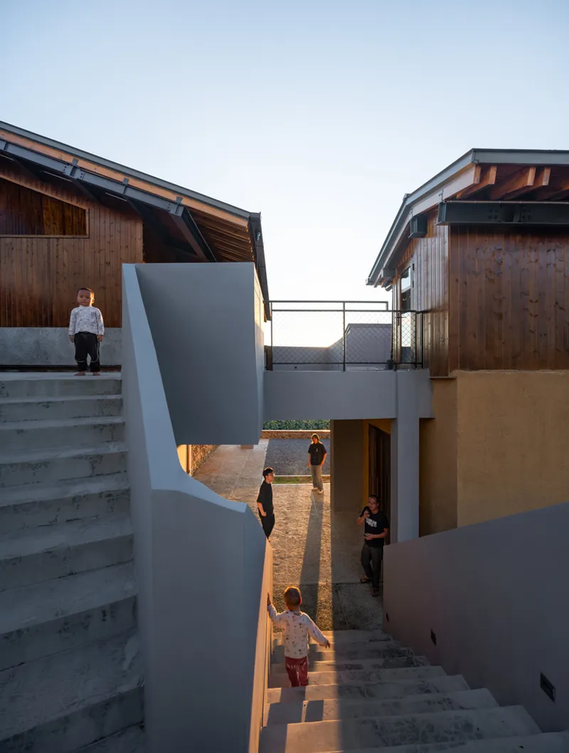 Outdoor staircase connecting split-level terraces between timber volumes with children playing at dusk