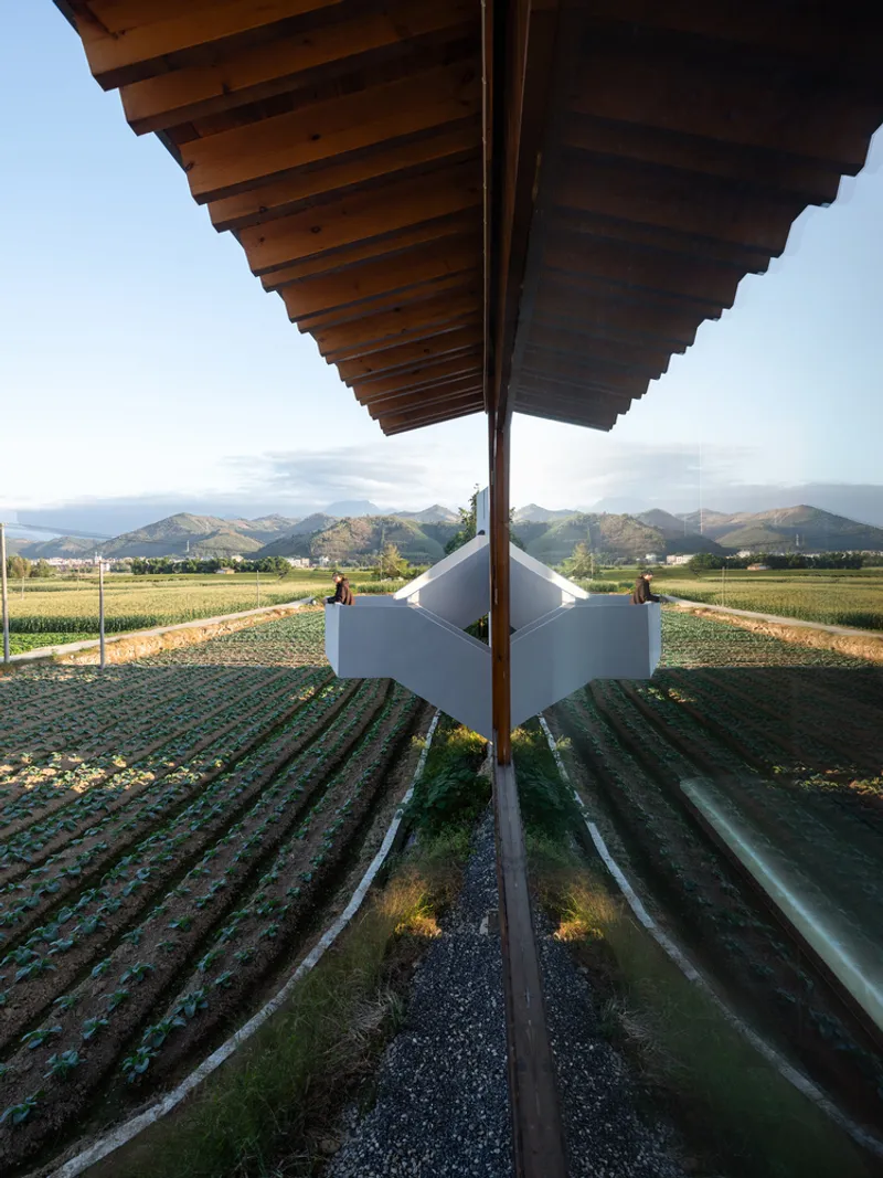 Symmetrical view beneath the timber roof canopy centered on a gravel path through cultivated fields