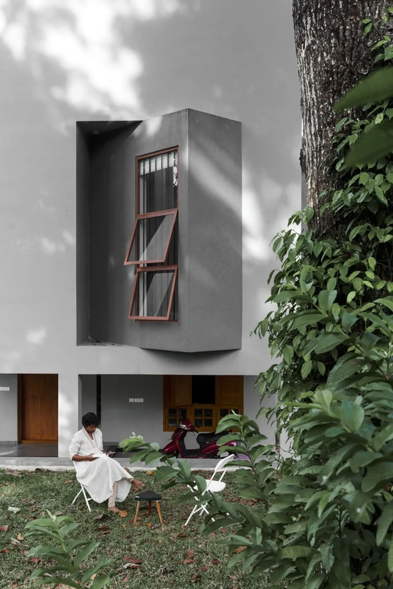 Projecting concrete box with angled timber windows beside a person seated in the garden